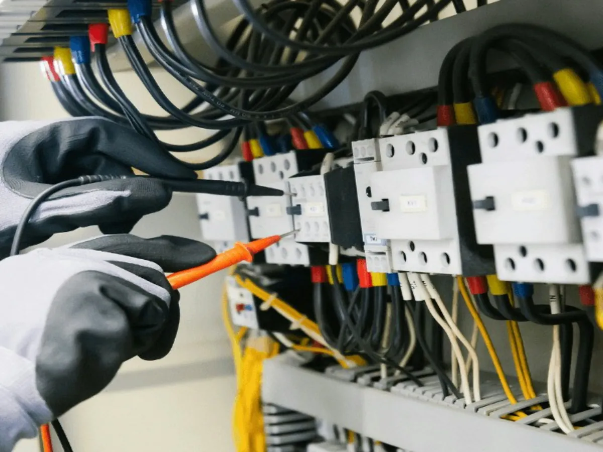 Eletricista de luvas testando um quadro de comando com multímetro
